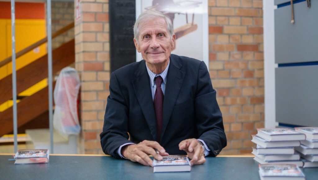 Ulrich Wickert lächelt in die Kamera, vor ihm seine Bücher